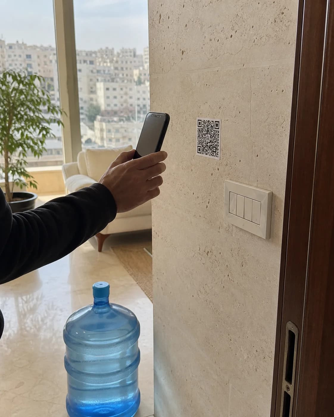 أحد أفراد البيت يمسح ملصق QR ثابت على حائط حجري في منزل بعمّان
